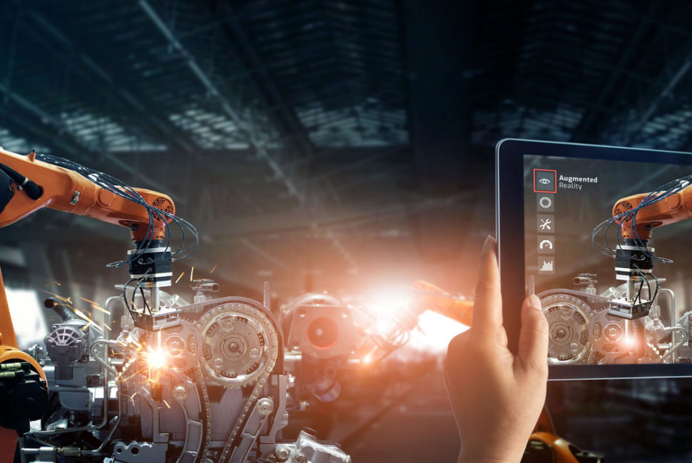 Augmented reality industry concept. Hand holding digital tablet use AR application to check and control welding robotics automatic arms machine in intelligent factory automotive industrial with monitoring system software. Digital manufacturing operation.
