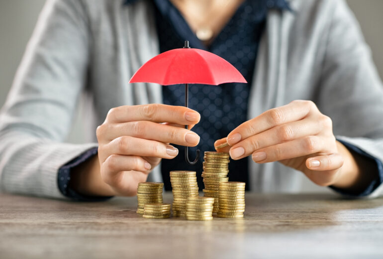 Hands protecting pile of coins with umbrella